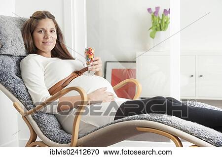 Pregnant woman lying in lounge chair and holding a glass filled with colorful candy on her stomach View Large Photo Image Stock Image - Pregnant woman lying in lounge chair and holding a glass filled with colorful candy on her stomach. Fotosearch
