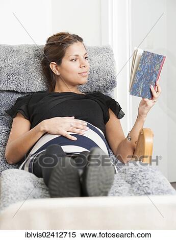 Stock Photography - Pregnant woman lying in lounge chair and reading a diary. Fotosearch