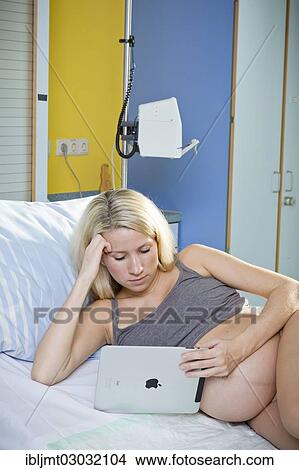 Picture - "Pregnant woman lying in the delivery room on the delivery bed and looking at a tablet PC, Germany, Europe". Fotosearch
