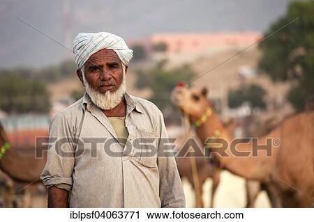 Stock Image - "Rajasthani wearing traditional dress with camel at the Pushkar Mela camel and livestock fair, Pushkar, Rajasthan, India, Asia". Fotosearch