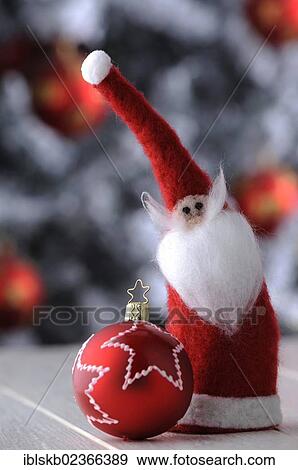 Stock Photo - Red Christmas bauble and a felt Santa Claus in front of a Christmas tree. Fotosearch