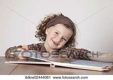 Stock Image - "Red-haired girl, 5 years old, sitting at the table with a children's book". Fotosearch