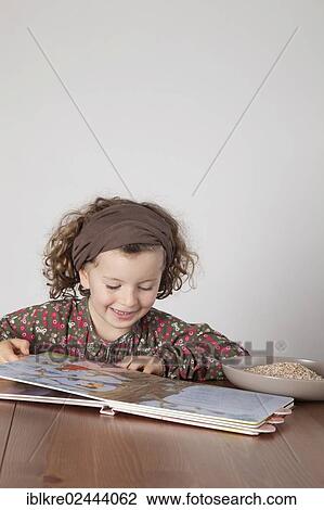 Stock Image - "Red-haired girl, 5 years old, sitting at the table reading a children's book". Fotosearch