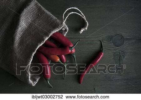 Stock Image - Red peppers in a jute sack lying on a wooden table. Fotosearch