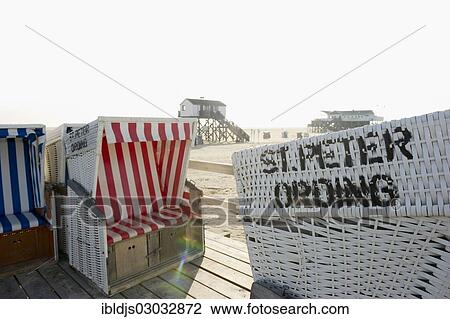 Stock Image - "Roofed wicker beach chairs on the beach in front of houses on stilts, St Peter-Ording, Schleswig-Holstein, Germany, Europe". Fotosearch