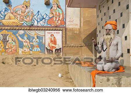 "Sadhu, a holy man or wandering ascetic sitting meditating on a towel, his body is smeared with white ashes in the sign of Shiva, on the wall are paintings of several deities and people, Varanasi, Uttar Pradesh, India, Asia" View Large Photo Image Stock Photograph - "Sadhu, a holy man or wandering ascetic sitting meditating on a towel, his body is smeared with white ashes in the sign of Shiva, on the wall are paintings of several deities and people, Varanasi, Uttar Pradesh, India, Asia". Fotosearch