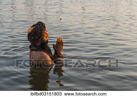 Stock Image - "Sadhu, holy man, taking a bath and praying in the Sangam, the confluence of the rivers Ganges, Yamuna and Saraswati, just before sunset, Kumbha Mela mass Hindu pilgrimage, Allahabad, Uttar Pradesh, India, Asia". Fotosearch