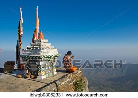 "Sadhu or holy man sitting with his hands folded in prayer on the precipice in front of a Hindu temple shrine with prayer flags, Tempelberg Shatrunjaya, Palitana, Gujarat, India, Asia" View Large Photo Image Stock Image - "Sadhu or holy man sitting with his hands folded in prayer on the precipice in front of a Hindu temple shrine with prayer flags, Tempelberg Shatrunjaya, Palitana, Gujarat, India, Asia". Fotosearch