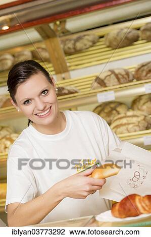 Stock Image - "Saleswoman in a bakery packing a bun in a bag, Austria, Europe". Fotosearch