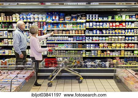 Stock Photo - "Senior couple shopping with a shopping trolley in the refrigerated dairy section in a supermarket, Germany, Europe". Fotosearch