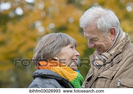 Stock Image - "Senior couple smiling at each other, in front of autumnal trees, Stadtpark, Berlin, Berlin, Germany, Europe". Fotosearch