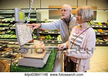 Stock Photograph - "Senior couple weighing fruit at the self-service scales while shopping in the fruit and vegetables department of a supermarket, Germany, Europe". Fotosearch