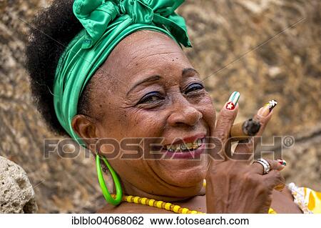 Stock Image - "Senior Cuban woman with the Cuban flag painted on her fingernail smoking a Cuban cigar, Havana, Cuba, North America". Fotosearch