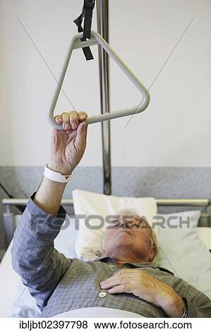 Stock Photo - "Senior in a hospital, holding a hand grip on a bed". Fotosearch
