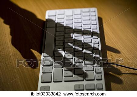Stock Image - Shadow of a hand on a computer keyboard. Fotosearch