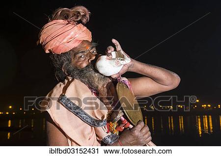 "Shiva sadhu, holy man, playing on a shell at night at the Sangam, the confluence of the rivers Ganges, Yamuna and Saraswati, during Kumbha Mela festival, Allahabad, Uttar Pradesh, India, Asia" View Large Photo Image Stock Image - "Shiva sadhu, holy man, playing on a shell at night at the Sangam, the confluence of the rivers Ganges, Yamuna and Saraswati, during Kumbha Mela festival, Allahabad, Uttar Pradesh, India, Asia". Fotosearch