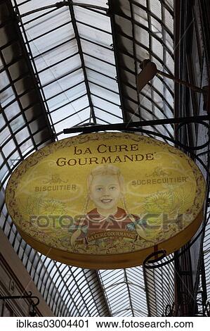 Stock Image - "Shop sign with the image of a girl, La Cure Gourmande candy store, historic shopping arcade, Passage Jouffroy, Grands Boulevards, 2nd Arrondissement, Paris, Ile-de-France, France, Europe". Fotosearch