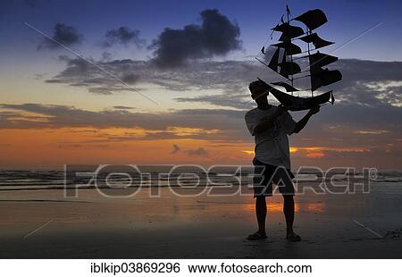 Stock Photograph - "Silhouette of a man holding a kite shaped like a ship, Sanur Beach, Bali, Indonesia, Asia". Fotosearch