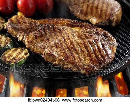 Stock Photo - Sirloin beef steaks and tomatoes being pan fried on a BBQ. Fotosearch