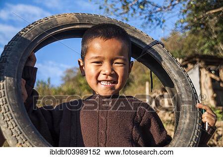 Stock Image - "Smiling boy from the Lahu people, hill tribe, ethnic minority, plays with a motorcycle tyre, Mae Hong Song Province, Northern Thailand, Thailand, Asia". Fotosearch