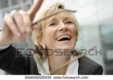 Picture - "Smiling business woman, 40-50, holding her glasses". Fotosearch