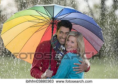 Smiling couple under a rainbow-coloured umbrella enjoying the rain View Large Photo Image Stock Image - Smiling couple under a rainbow-coloured umbrella enjoying the rain. Fotosearch