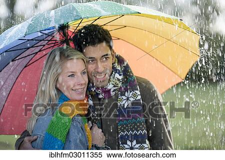 Smiling couple with a colourful rainbow umbrella is enjoying the rain View Large Photo Image Stock Photography - Smiling couple with a colourful rainbow umbrella is enjoying the rain. Fotosearch