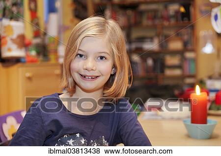 Stock Photo - "Smiling girl, 9, sitting at a table with a candle". Fotosearch