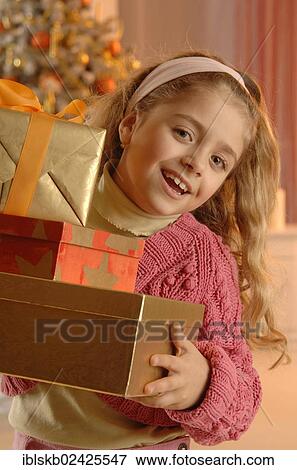 Stock Photo - Smiling girl holding several gifts in front of a Christmas tree. Fotosearch