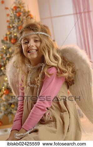 Smiling girl wearing a dress with angel wings in front of a Christmas tree View Large Photo Image Stock Photo - Smiling girl wearing a dress with angel wings in front of a Christmas tree. Fotosearch