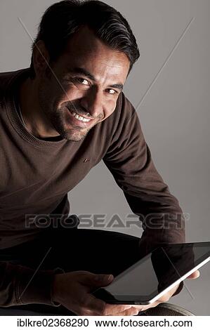 Stock Image - Smiling man holding an iPad. Fotosearch