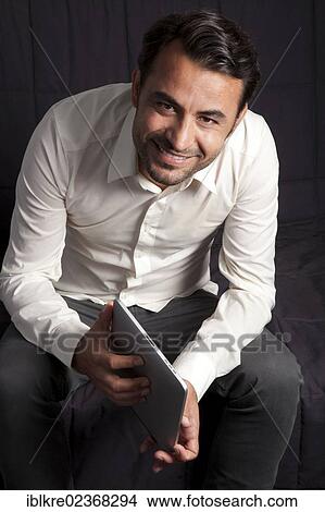 Smiling man sitting on a sofa with an iPad View Large Photo Image Picture - Smiling man sitting on a sofa with an iPad. Fotosearch