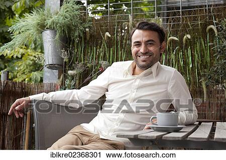 Smiling man sitting with a coffee cup on the balcony View Large Photo Image Stock Image - Smiling man sitting with a coffee cup on the balcony. Fotosearch