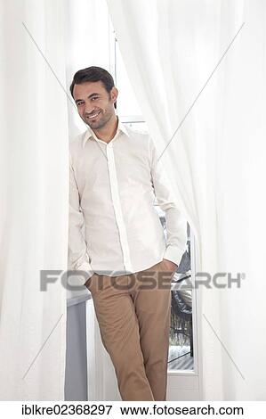 Stock Photo - Smiling man standing at a balcony door with curtains. Fotosearch