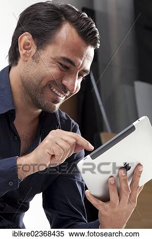 Smiling man using an iPad View Large Photo Image Stock Photography - Smiling man using an iPad. Fotosearch