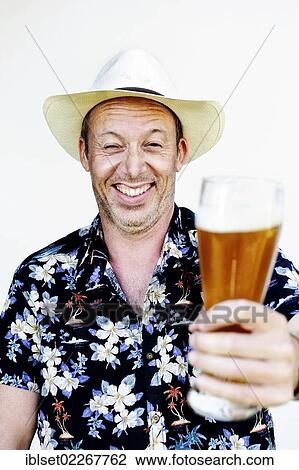 Stock Image - Smiling man wearing a straw hat and a Hawaiian shirt holding a wheat beer. Fotosearch