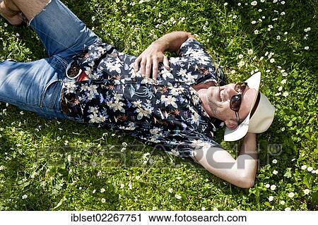 "Smiling man wearing a straw hat, sunglasses and a Hawaiian shirt, lying in a flowering meadow, has a blade of grass in his mouth" View Large Photo Image Stock Image - "Smiling man wearing a straw hat, sunglasses and a Hawaiian shirt, lying in a flowering meadow, has a blade of grass in his mouth". Fotosearch