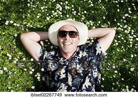 "Smiling man wearing a straw hat, sunglasses and a Hawaiian shirt, lying in a flowering meadow, has a daisy in his mouth" View Large Photo Image Stock Photo - "Smiling man wearing a straw hat, sunglasses and a Hawaiian shirt, lying in a flowering meadow, has a daisy in his mouth". Fotosearch