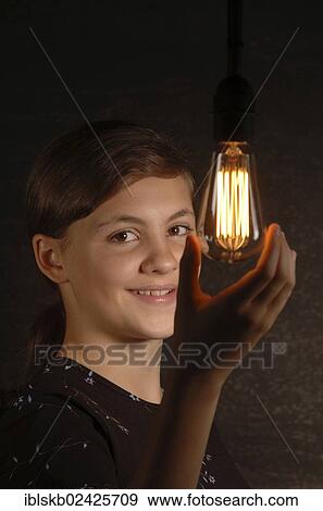Stock Photo - Smiling teenage girl holding a glowing light bulb in her hand. Fotosearch