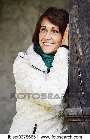 Stock Image - Smiling woman leaning on a wooden post. Fotosearch