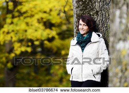 Picture - Smiling woman standing at a tree in autumn. Fotosearch
