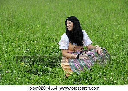 Picture - "Smiling woman wearing a dirndl dress, sitting in a meadow in Tyrol, Austria, Europe". Fotosearch