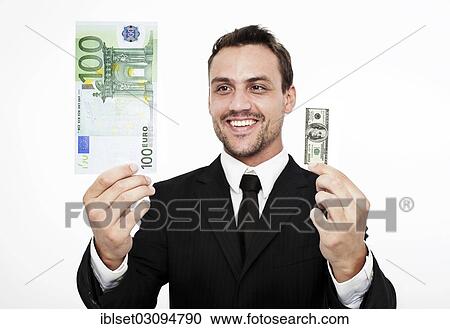 Stock Image - "Smiling young man wearing a suit holding a large 100 euro banknote and a small 100 dollar bill, Austria, Europe". Fotosearch