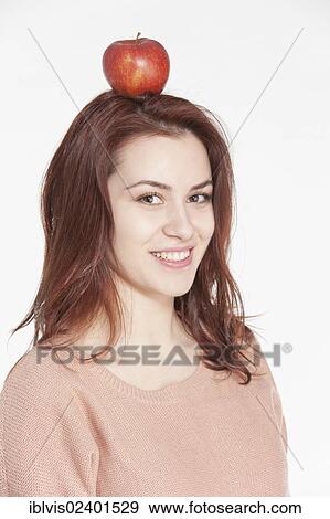 Stock Photo - Smiling young woman balancing apple on her head. Fotosearch
