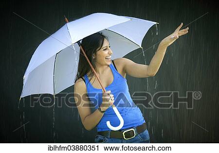 Stock Image - "Smiling young woman holding an umbrella, enjoying the rain". Fotosearch