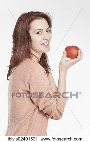 Stock Image - Smiling young woman holding apple. Fotosearch