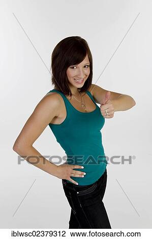 Stock Image - Smiling young woman making thumbs up gesture. Fotosearch