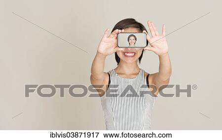 Smiling young woman taking a self portrait with the mobile phone View Large Photo Image Stock Photo - Smiling young woman taking a self portrait with the mobile phone. Fotosearch