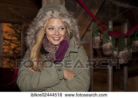Smiling young woman wearing a green parka standing with her arms crossed in front of a hiking hut decorated for Christmas View Large Photo Image Stock Photo - Smiling young woman wearing a green parka standing with her arms crossed in front of a hiking hut decorated for Christmas. Fotosearch