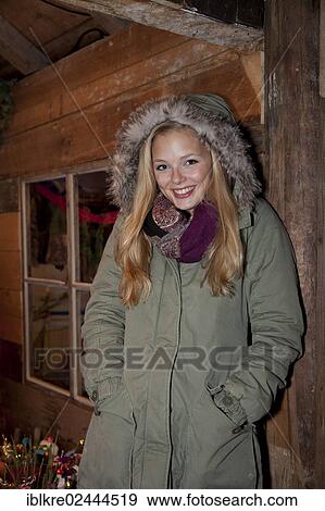 Smiling young woman wearing a green parka standing in front of a hiking hut decorated for Christmas View Large Photo Image Stock Photo - Smiling young woman wearing a green parka standing in front of a hiking hut decorated for Christmas. Fotosearch